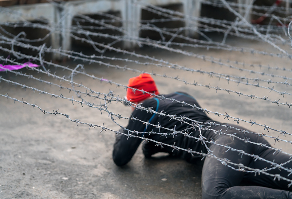 Men waering a wetsuit under the barb wire obstacle
